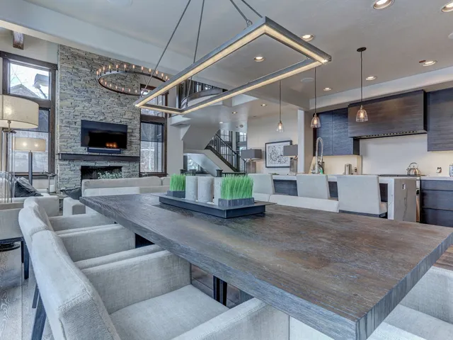 Dining table under a modern linear light fixture near an open kitchen